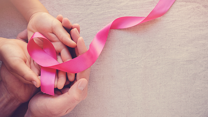 Two women hold a pink ribbon for breast cancer and reconstruction