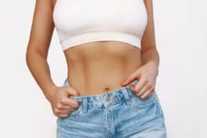 Woman with slim, toned abs from tummy tuck wearing jeans and crop top